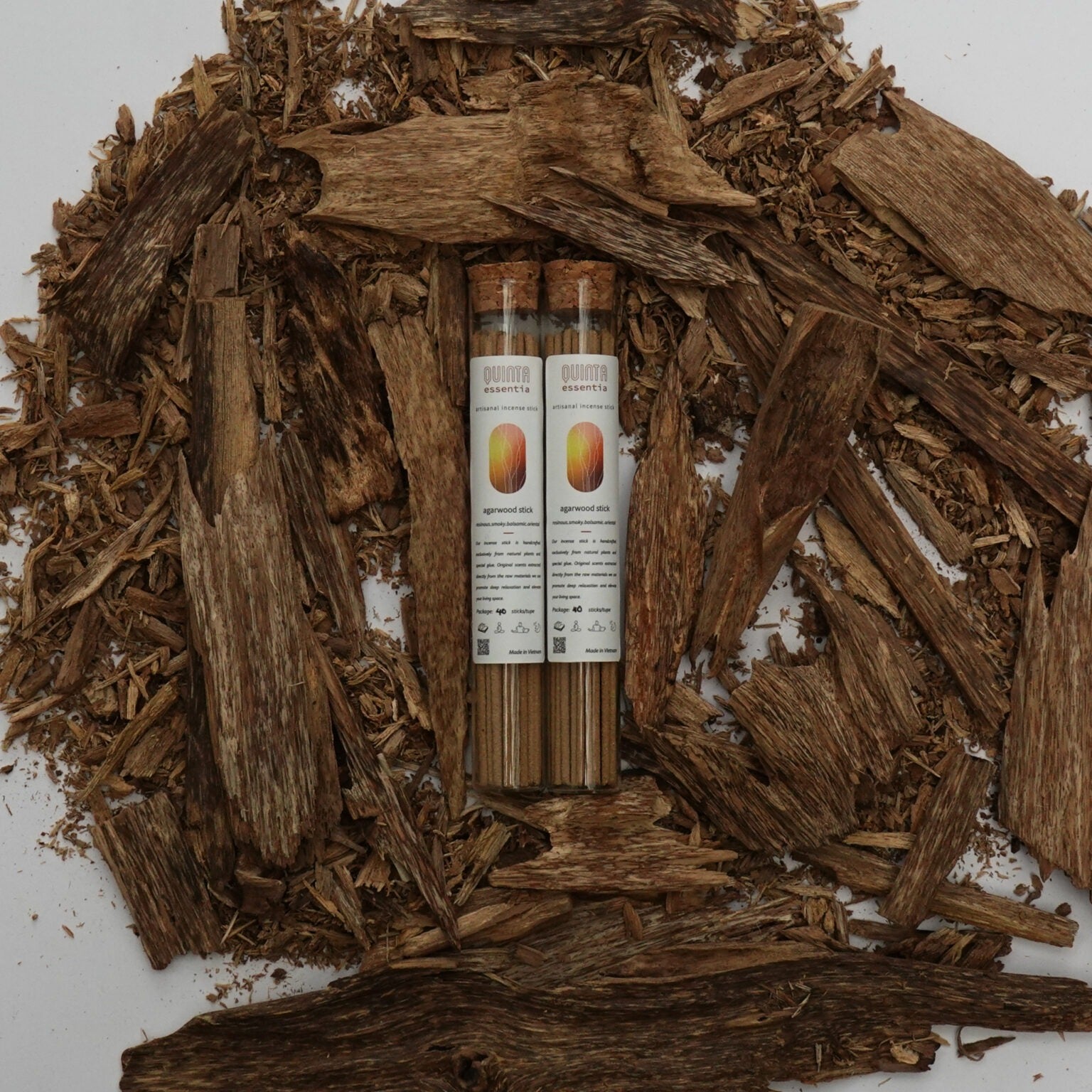 Two bottles of Agarwood incense surrounded by Agarwood chips on a white background