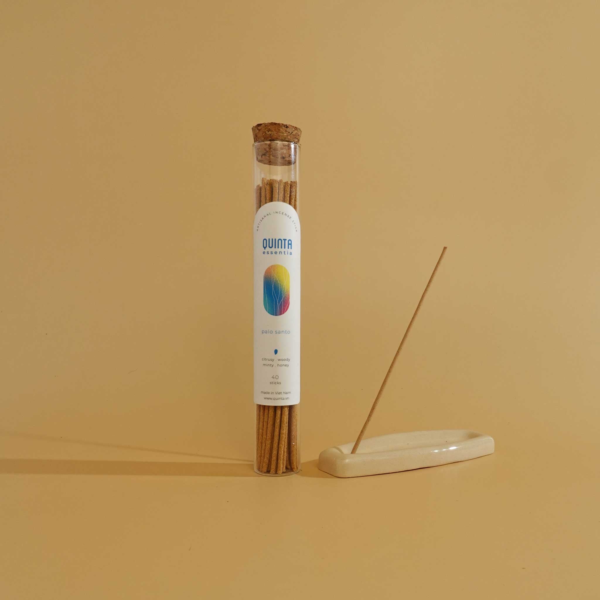 Tube of Palo Santo incense sticks with a single Palo Santo incense stick on a beige surface