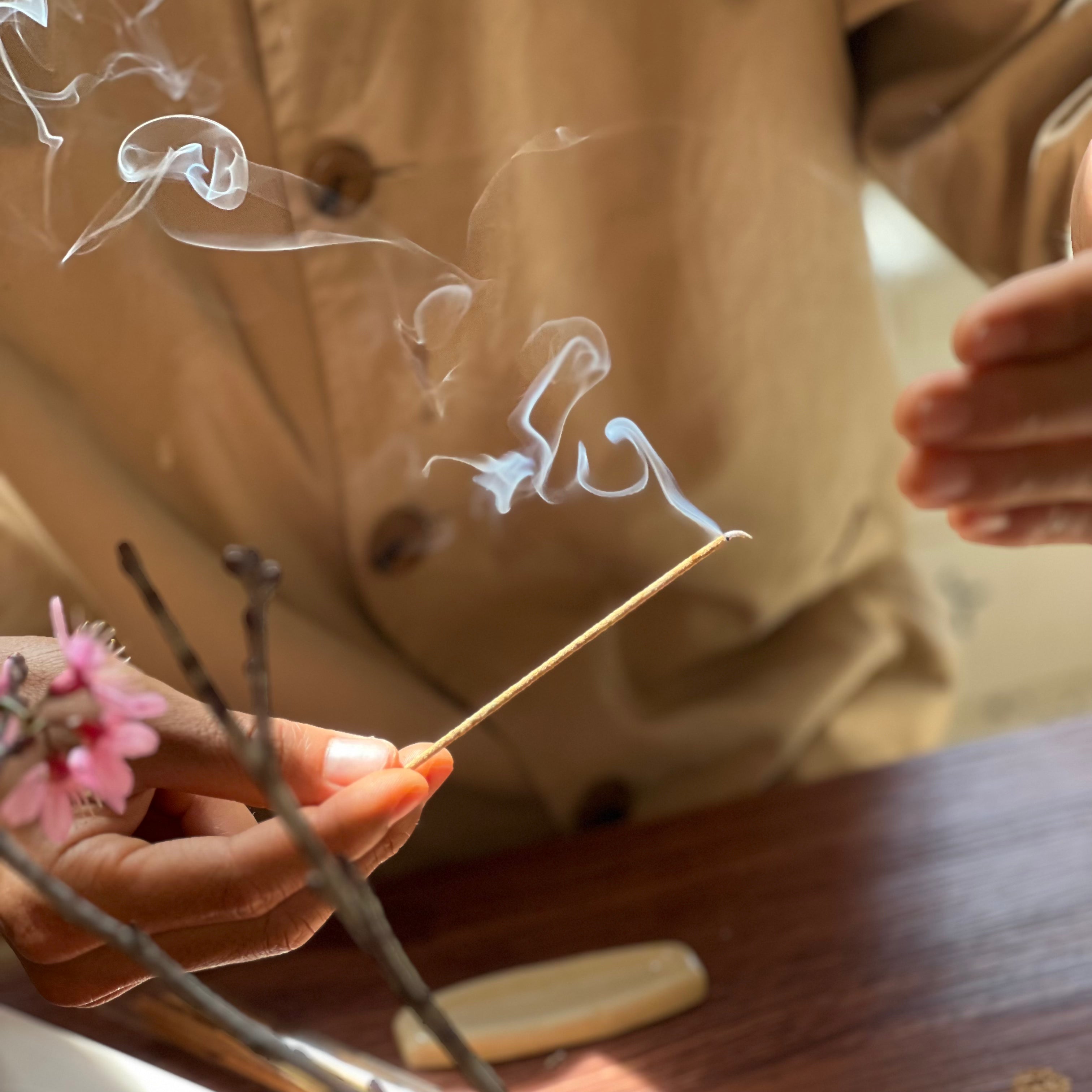 Person holding a burning incense stick with smoke and a blurred background