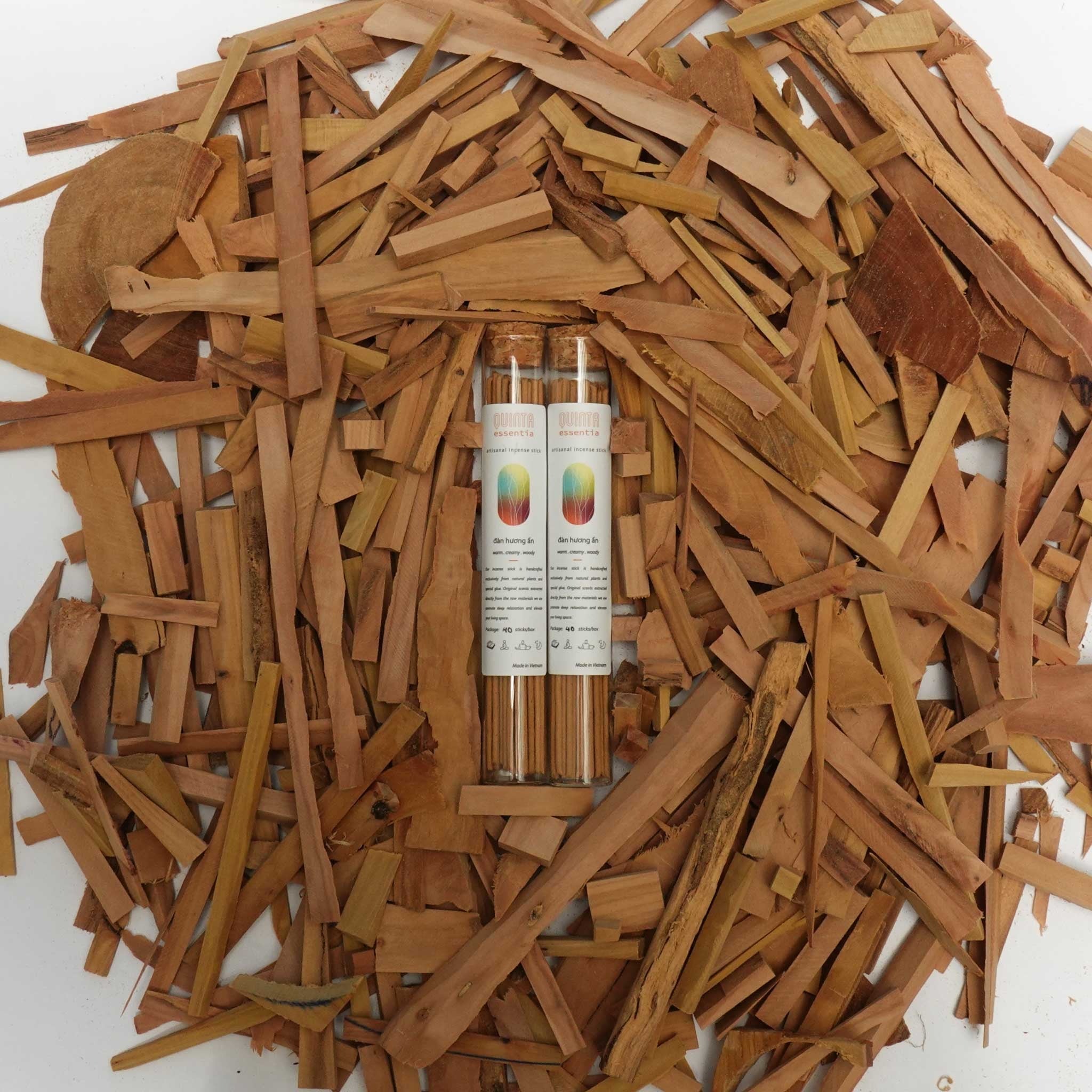 Two small bottles of sandalwood incense with labels surrounded by sandalwood sticks on a white background
