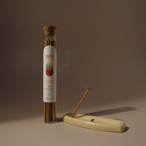 Sandalwood incense stick tube with a lit sandalwood incense stick on a beige stand against a brown background